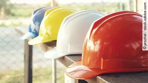Vier Bauarbeiterhelme liegen nebeneinander auf einem Geländer.
