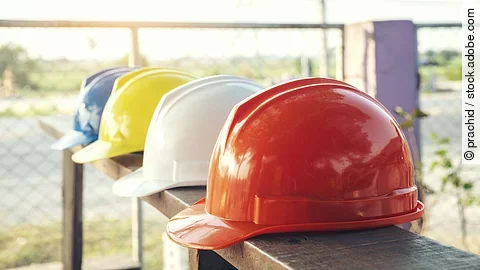 Baustelle Vier Bauarbeiterhelme liegen nebeneinander auf einem Geländer.
