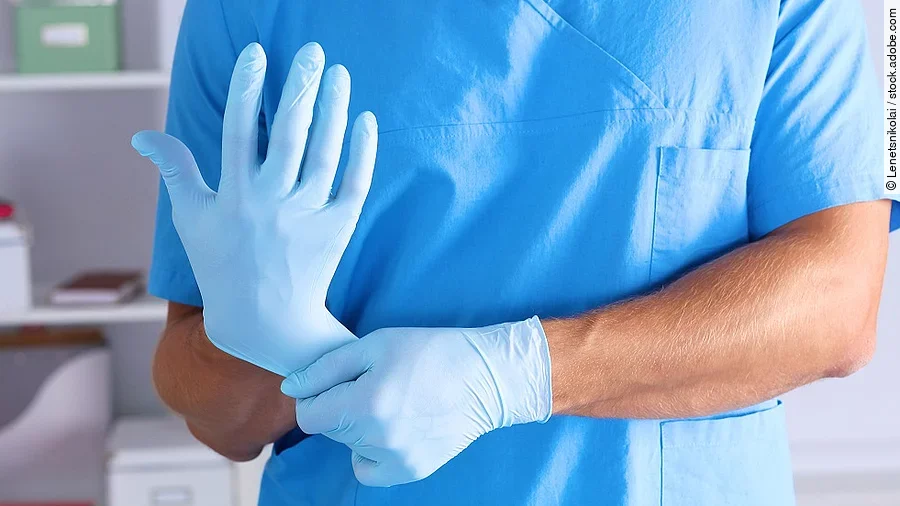 Eine Person im Kasack zieht sich blaue Schutzhandschuhe über.