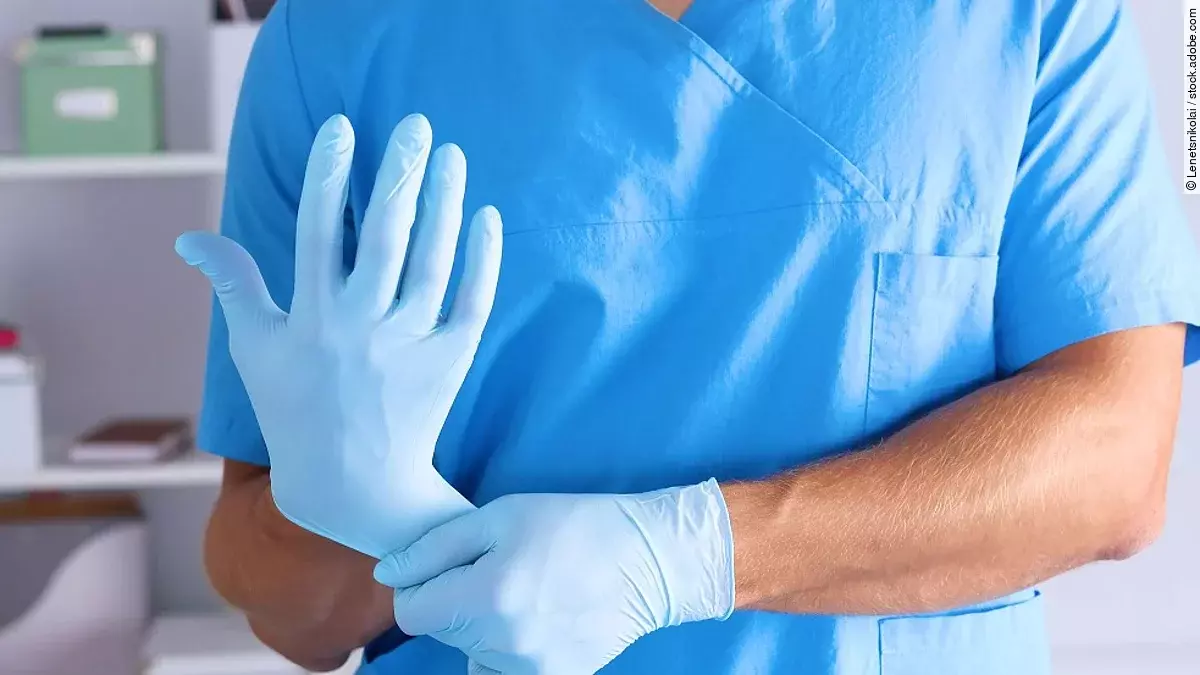Arzt mit Handschuhen Eine Person im Kasack zieht sich blaue Schutzhandschuhe über.
