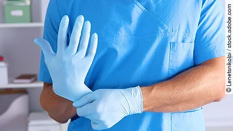 Eine Person im Kasack zieht sich blaue Schutzhandschuhe über.