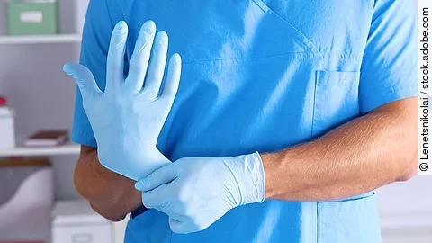 Eine Person im Kasack zieht sich blaue Schutzhandschuhe über.