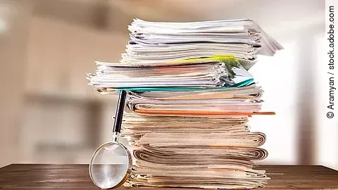 Auf einem Tisch liegt ein Stapel mit Unterlagen und daneben eine Lupe.