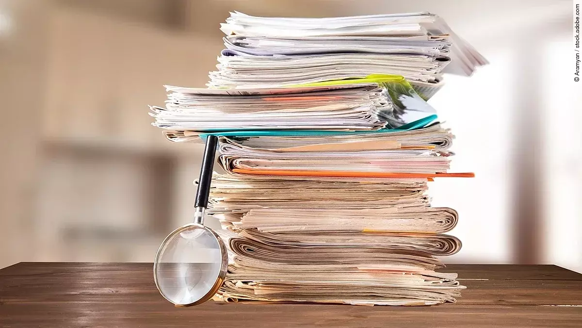 Dokumente Auf einem Tisch liegt ein Stapel mit Unterlagen und daneben eine Lupe.