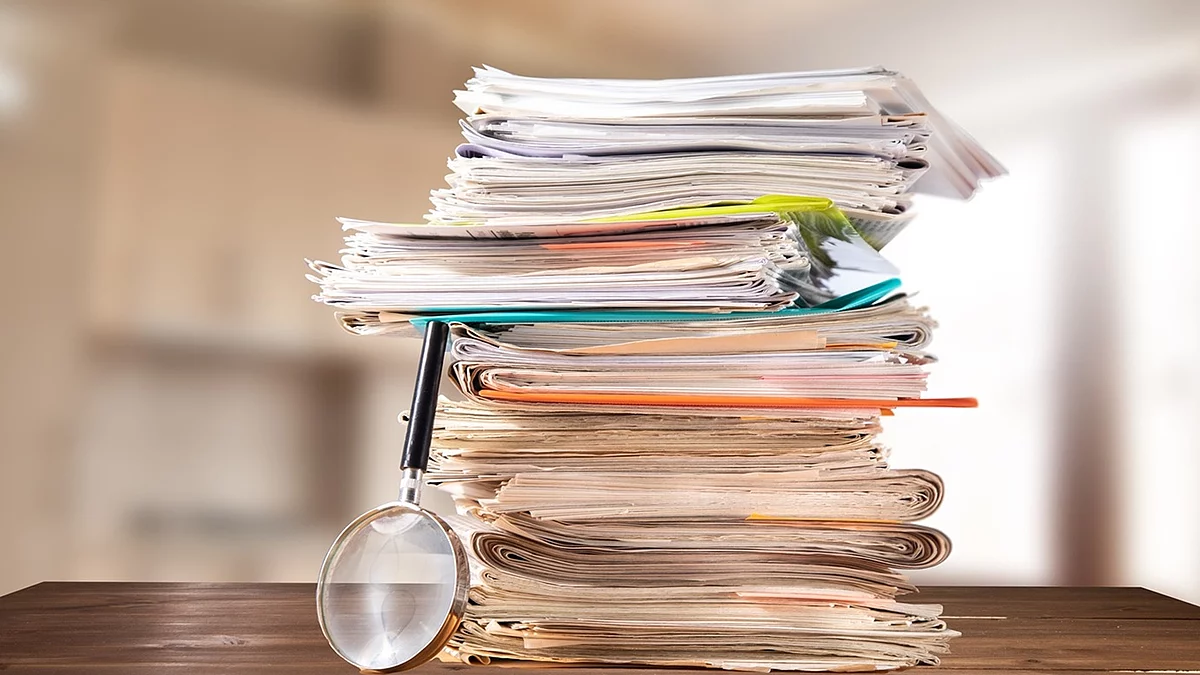 Dokumente Auf einem Tisch liegt ein Stapel mit Unterlagen und daneben eine Lupe.