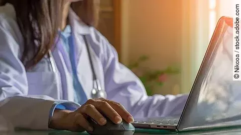 Ärztin sitzt vor dem Computer in weißem Kittel.