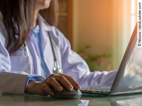 Ärztin sitzt vor dem Computer in weißem Kittel.