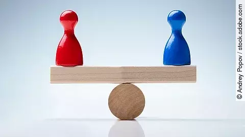 Auf einer holzähnlichen Waage stehen eine rote und blaue Figur, die das Gleichgewicht halten. 