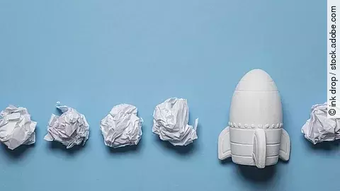 In einer Reihe liegen zusammengeknüllte Blätter Papier. Rechts in der Reihe liegt statt einem Papier eine kleine weiße Rakete.