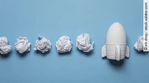 In einer Reihe liegen zusammengeknüllte Blätter Papier. Rechts in der Reihe liegt statt einem Papier eine kleine weiße Rakete.