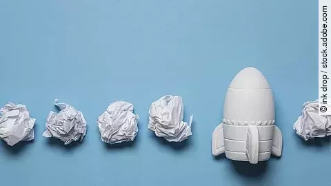 In einer Reihe liegen zusammengeknüllte Blätter Papier. Rechts in der Reihe liegt statt einem Papier eine kleine weiße Rakete.