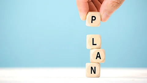 Hand stapelt vier Holzwürfel mit Buchstaben die das Wort Plan ergeben.