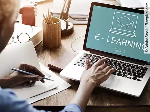Eine Frau sitzt vor einem aufgeklappten Laptop, auf dem Bildschirm steht "E-Learning".