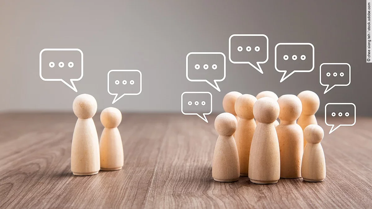 Debatte Mehrere Holz-Spielfiguren mit Sprechblasen.