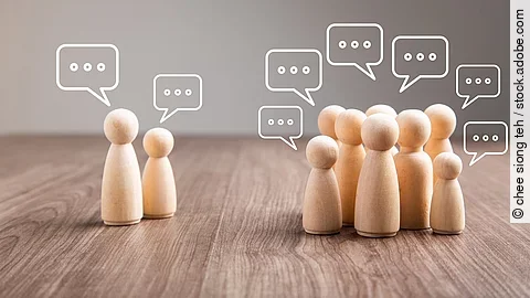 Debatte Mehrere Holz-Spielfiguren mit Sprechblasen.