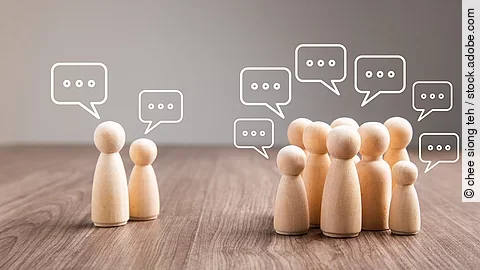 Debatte Mehrere Holz-Spielfiguren mit Sprechblasen.