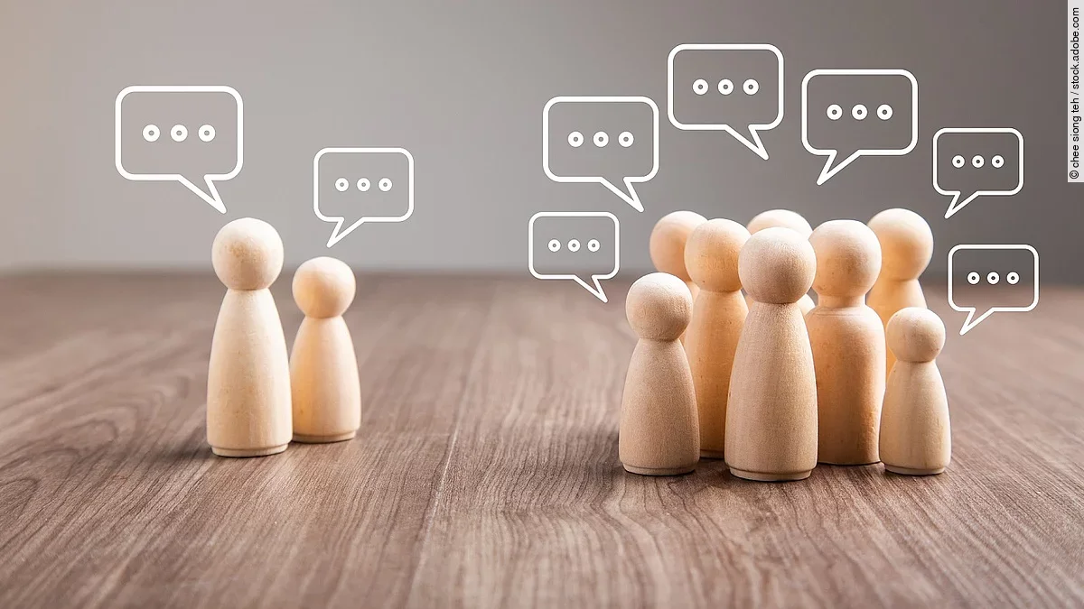 Debatte Mehrere Holz-Spielfiguren mit Sprechblasen.