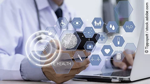 E-Health Ein Arzt hält ein Tablet in den Händen. Über dem Gerät schweben Symbole und Icons in einer hologrammartigen Darstellung.