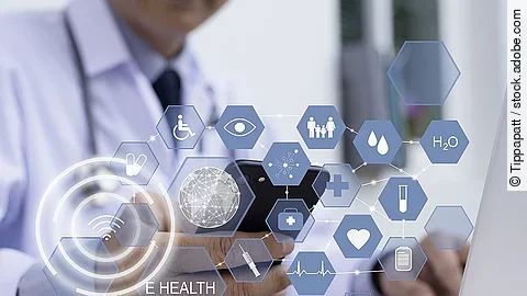 E-Health Ein Arzt hält ein Tablet in den Händen. Über dem Gerät schweben Symbole und Icons in einer hologrammartigen Darstellung.