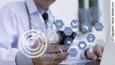 E-Health Ein Arzt hält ein Tablet in den Händen. Über dem Gerät schweben Symbole und Icons in einer hologrammartigen Darstellung.