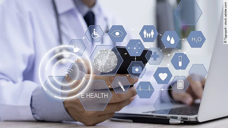 E-Health Ein Arzt hält ein Tablet in den Händen. Über dem Gerät schweben Symbole und Icons in einer hologrammartigen Darstellung.