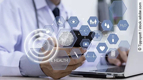 E-Health Ein Arzt hält ein Tablet in den Händen. Über dem Gerät schweben Symbole und Icons in einer hologrammartigen Darstellung.