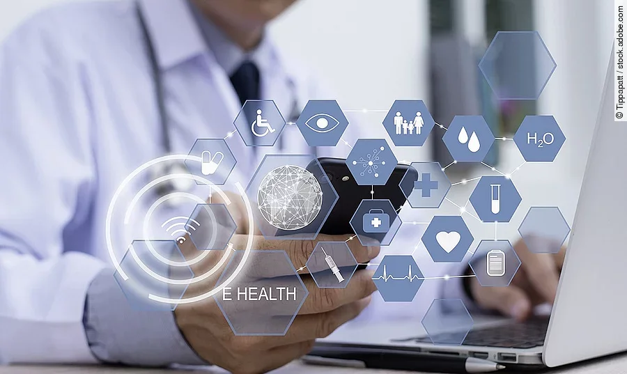 E-Health Ein Arzt hält ein Tablet in den Händen. Über dem Gerät schweben Symbole und Icons in einer hologrammartigen Darstellung.