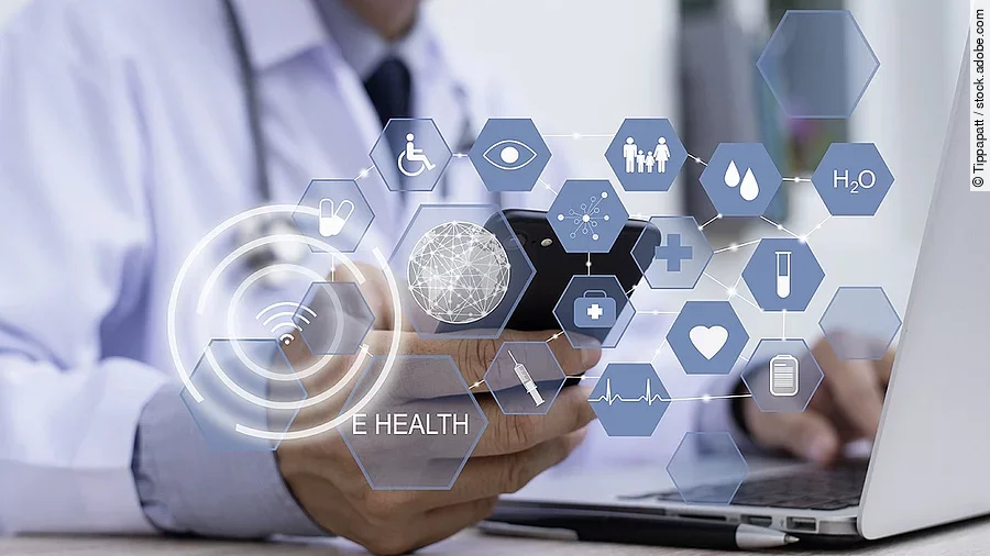E-Health Ein Arzt hält ein Tablet in den Händen. Über dem Gerät schweben Symbole und Icons in einer hologrammartigen Darstellung.