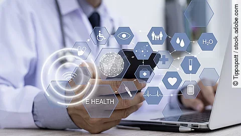 E-Health Ein Arzt hält ein Tablet in den Händen. Über dem Gerät schweben Symbole und Icons in einer hologrammartigen Darstellung.