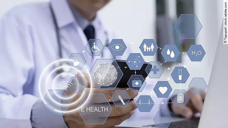 E-Health Ein Arzt hält ein Tablet in den Händen. Über dem Gerät schweben Symbole und Icons in einer hologrammartigen Darstellung.