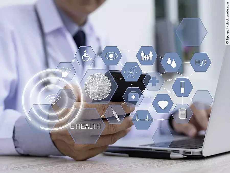 E-Health Ein Arzt hält ein Tablet in den Händen. Über dem Gerät schweben Symbole und Icons in einer hologrammartigen Darstellung.