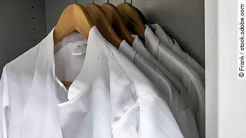 Arztkittel Mehrere Arztkittel hängen auf braunen Kleiderbügeln im Schrank.