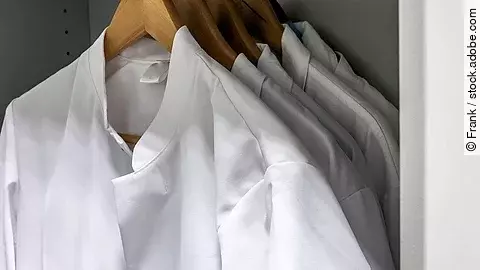 Arztkittel Mehrere Arztkittel hängen auf braunen Kleiderbügeln im Schrank.