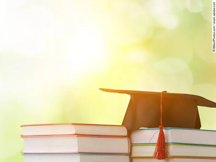 Ein schwarzer Absolventenhut liegt auf zwei Bücherstapeln.