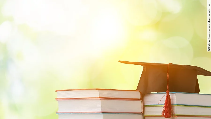 Ein schwarzer Absolventenhut liegt auf zwei Bücherstapeln.