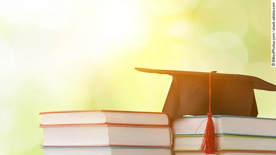 Ein schwarzer Absolventenhut liegt auf zwei Bücherstapeln.