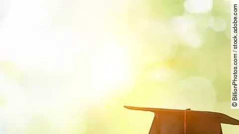 Ein schwarzer Absolventenhut liegt auf zwei Bücherstapeln.