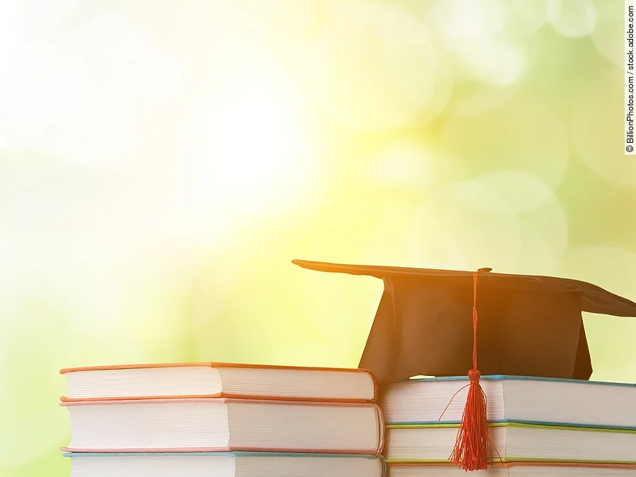 Ein schwarzer Absolventenhut liegt auf zwei Bücherstapeln.