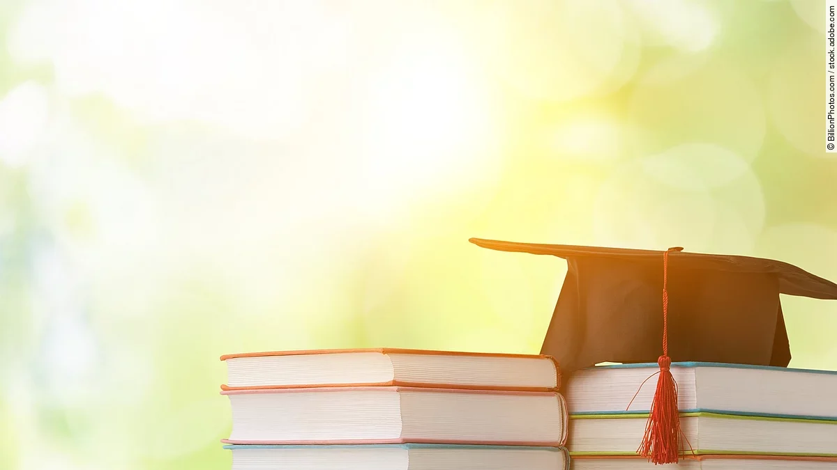 Ein schwarzer Absolventenhut liegt auf zwei Bücherstapeln.