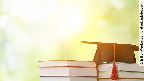 Ein schwarzer Absolventenhut liegt auf zwei Bücherstapeln.