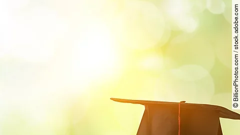 Ein schwarzer Absolventenhut liegt auf zwei Bücherstapeln.