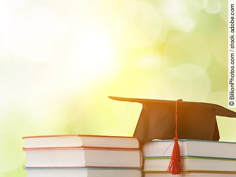 Ein schwarzer Absolventenhut liegt auf zwei Bücherstapeln.