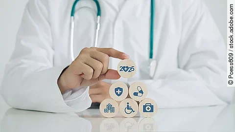 Gesundheitsversorgung Arzt mit Kittel und Stethoskop setzt Holzwürfel mit Aufschrift 2025 auf andere Würfel mit Medizin-Symbolen