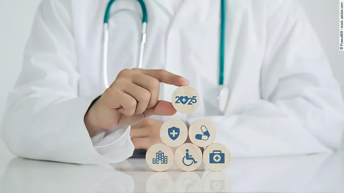 Gesundheitsversorgung Arzt mit Kittel und Stethoskop setzt Holzwürfel mit Aufschrift 2025 auf andere Würfel mit Medizin-Symbolen