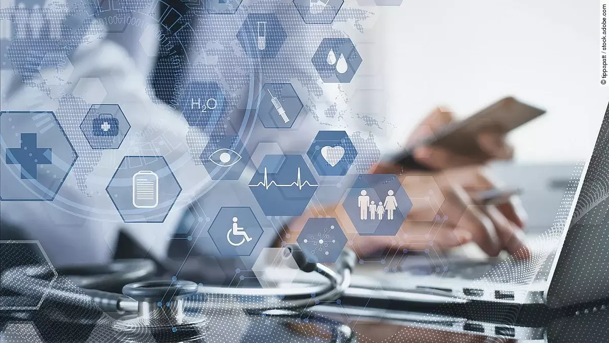 Ein Mann sitzt an seinem Laptop. Daneben liegt ein Stethoskop. Im Vordergrund erscheint eine holografische Darstellung aus vielen einzelnen Icons und Symbolen, die ein digitales Netzwerk aus Daten verkörpern sollen.