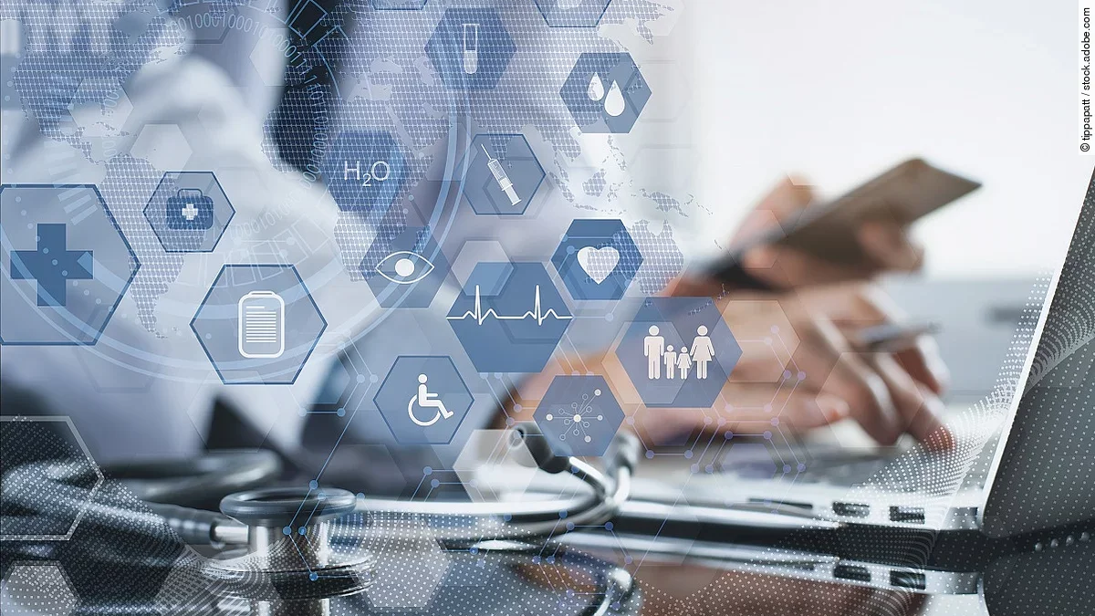 Ein Mann sitzt an seinem Laptop. Daneben liegt ein Stethoskop. Im Vordergrund erscheint eine holografische Darstellung aus vielen einzelnen Icons und Symbolen, die ein digitales Netzwerk aus Daten verkörpern sollen.