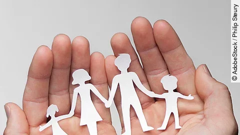 Schutz Zwei Hände bilden eine Schale, darin sind die Umrisse einer Familie mit Mutter, Vater und zwei Kindern zu sehen.