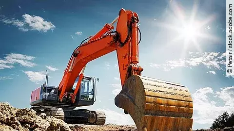 Ein organe-farbener Bagger steht auf einem Schutthaufen.