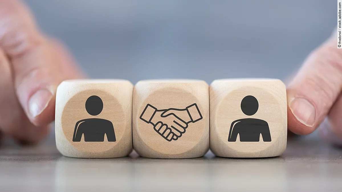 Holzwürfel auf denen zwei Personen und ein Handschlag abgebildet sind.