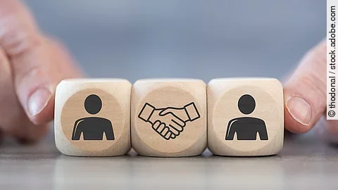 Holzwürfel auf denen zwei Personen und ein Handschlag abgebildet sind.
